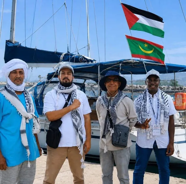 Four men wearing keffiyehs in front of a sailboat flying Palestinian and Mauritanian flags, file photo of Sumud flotilla participants