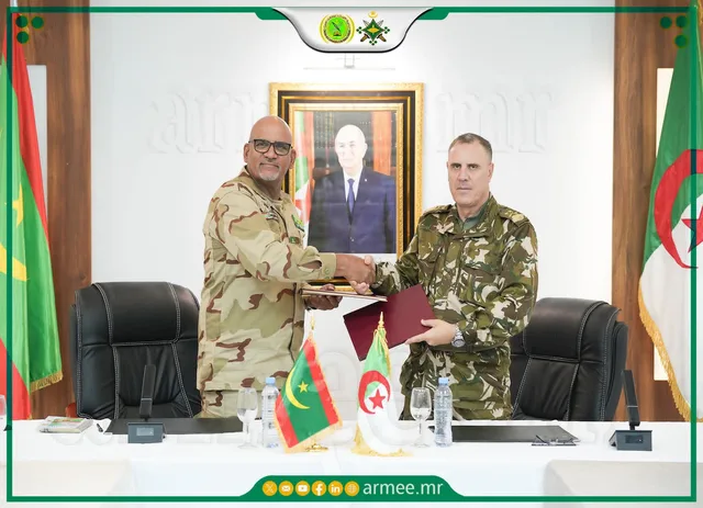 A Mauritanian and an Algerian officer exchange documents with both countries' flags on the table