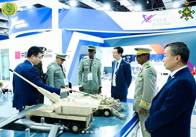 Officers look at armoured vehicle models at a stand of an international defence exhibition