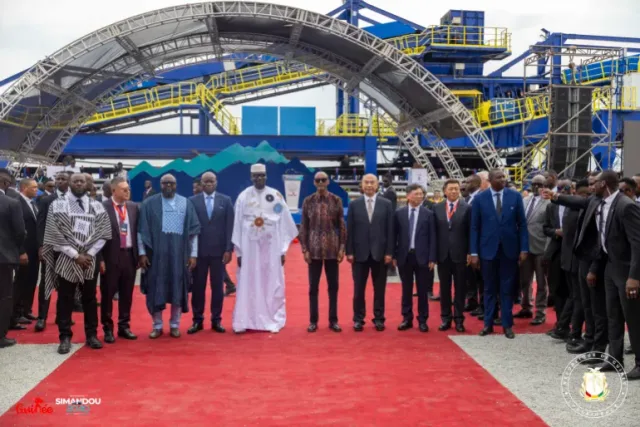 Officials stand on a red carpet in front of industrial installations at the launch of Guinea's Simandou mining project