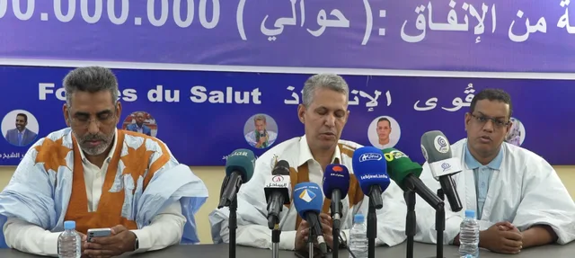 MP Mohamed Lemine Sidi Maouloud speaks into microphones, flanked by two Forces of Salvation coalition officials