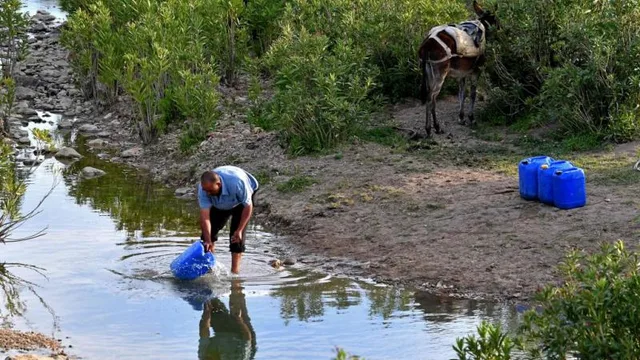 A man fills blue plastic jerrycans with water from a stream in Tunisia