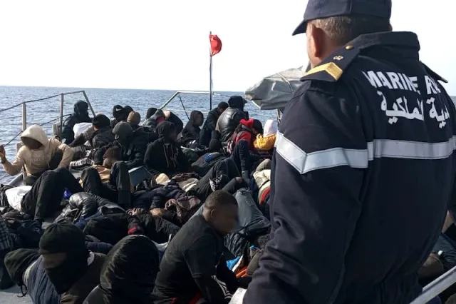 A Moroccan Royal Navy sailor next to a group of migrants on board a vessel at sea, file photo