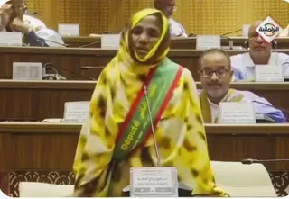 A woman MP wearing a parliamentary sash speaks in the National Assembly