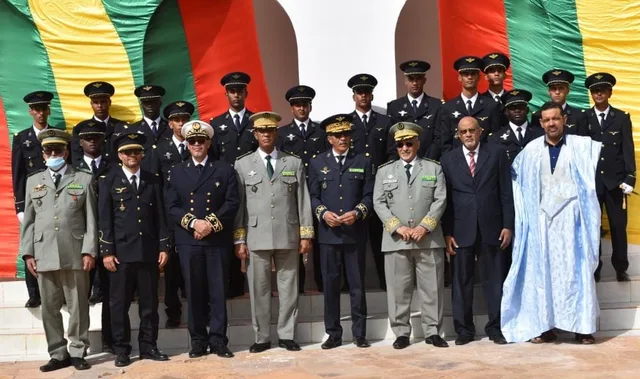 Officers and officials pose for a group photo in front of the Mauritanian flag