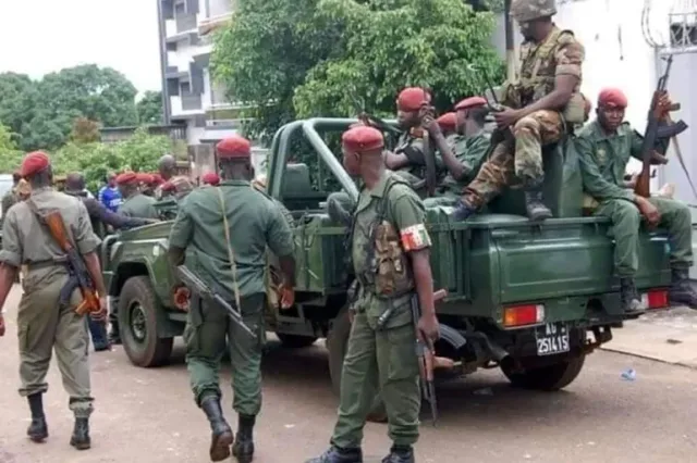 Armed Guinean soldiers in red berets around a green military vehicle in a street, file photo