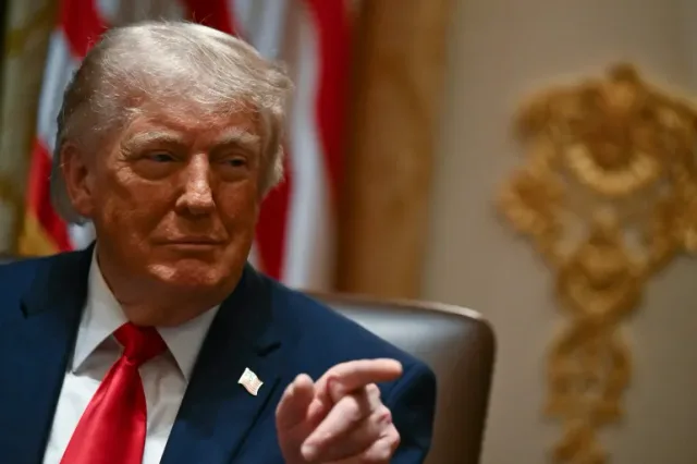 US President Donald Trump, seated, points in front of the US flag, file photo