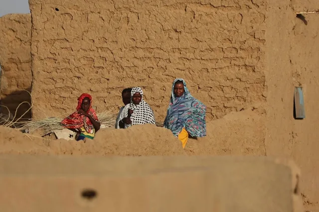 Women and children in front of a mud-brick wall in a town in northern Mali
