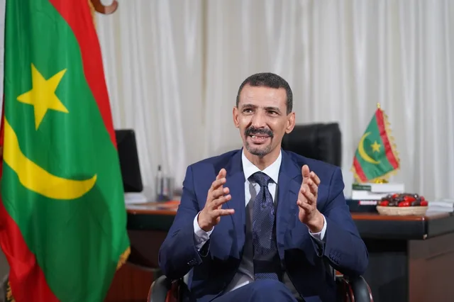 El Houssein Ould Meddou speaking in his office in front of the Mauritanian flag