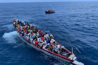 A boat crowded with migrants at sea, near a rescue vessel