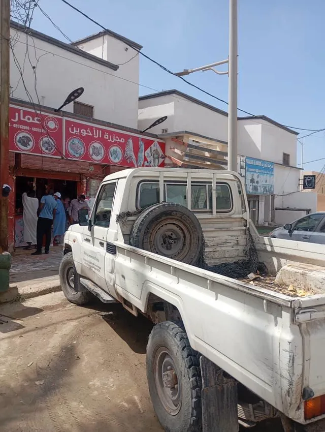 A white pickup parked outside a butcher's shop with a red sign in Nouakchott