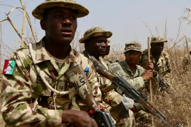 Nigerian soldiers in camouflage and bush hats holding rifles among dry grass during an exercise, file photo
