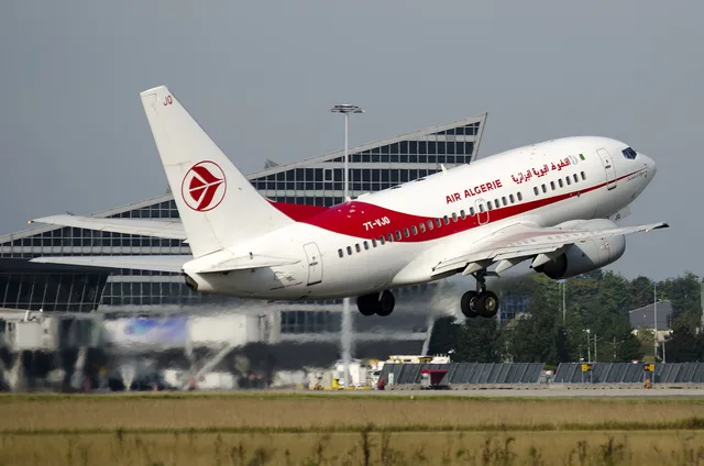 A white and red Air Algérie aircraft taking off from an airport runway