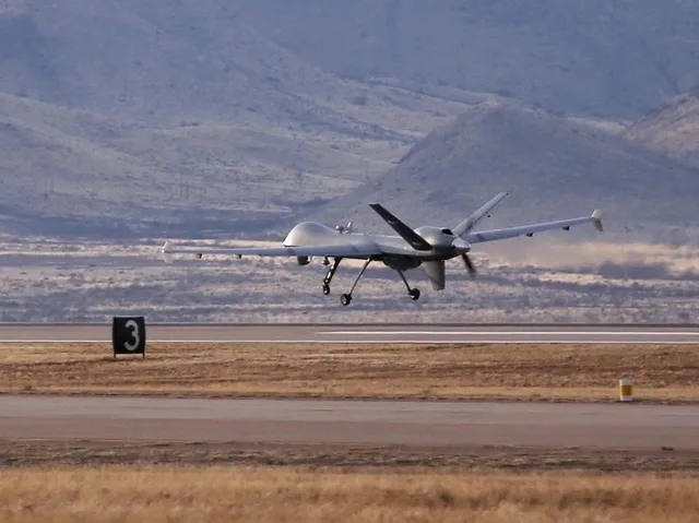 A grey military drone flying low over a runway surrounded by hills, illustrative file image