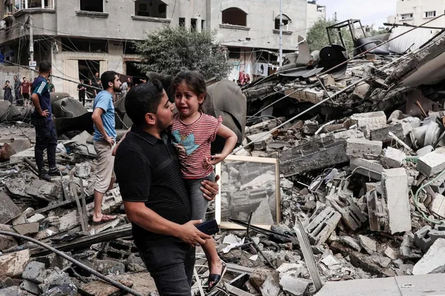 A man carries a crying girl through the rubble of a destroyed building in Gaza, file photo from October 2023