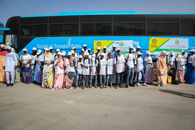A group of children in white T-shirts and caps standing in front of a public transport bus in Nouakchott