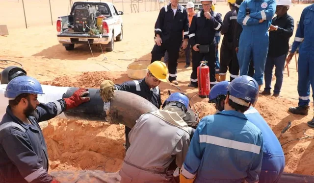 Workers in helmets and overalls fitting a pipe in a trench on sandy desert ground, file photo
