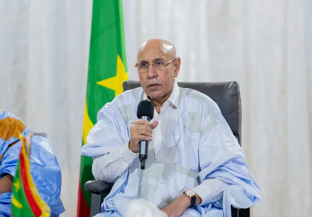 Mauritania's president speaks into a microphone at a meeting in front of the national flag