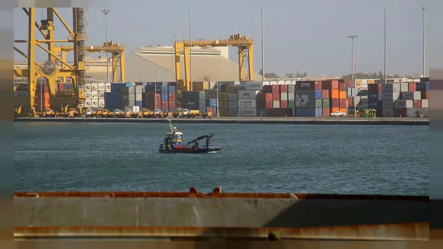 Containers and gantry cranes on a quay at the port of Dakar, with a small boat on the water