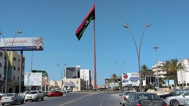 A tall flagpole flying the Libyan flag at the centre of a roundabout surrounded by cars, buildings and billboards, file photo