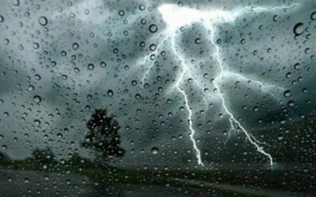 Lightning in a cloudy sky behind glass covered in raindrops, illustrative image
