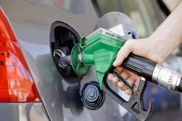A hand holding a green fuel pump nozzle in a car tank, file photo
