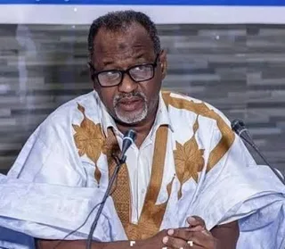 A union official in a white boubou speaking into microphones