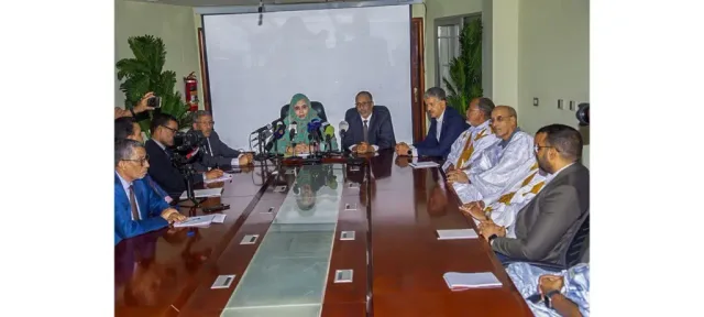 The trade and tourism minister seated among officials at a table with microphones