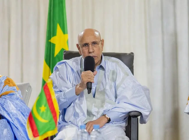 Mauritania's president speaks into a microphone at a meeting beside the national flag