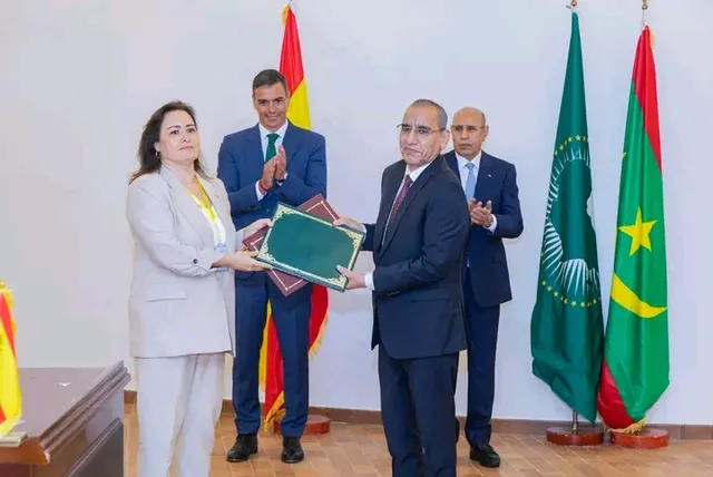 Presidents Ghazouani and Sanchez applaud as a Mauritanian official and a Spanish official exchange documents