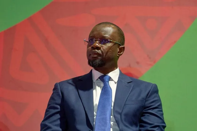 Ousmane Sonko in a blue suit against a red and green background