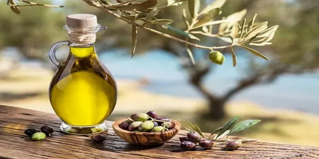 A glass bottle of olive oil and a wooden bowl of olives on a table, file photo
