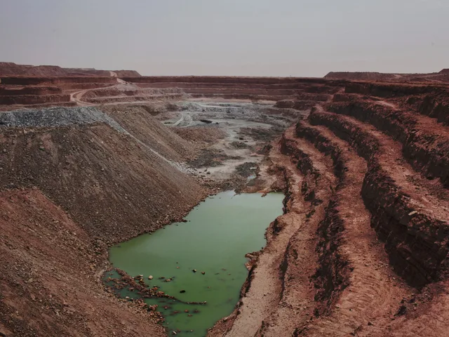 A vast open-pit mine with red earth terraces and a green pool at the bottom, in the desert, file photo