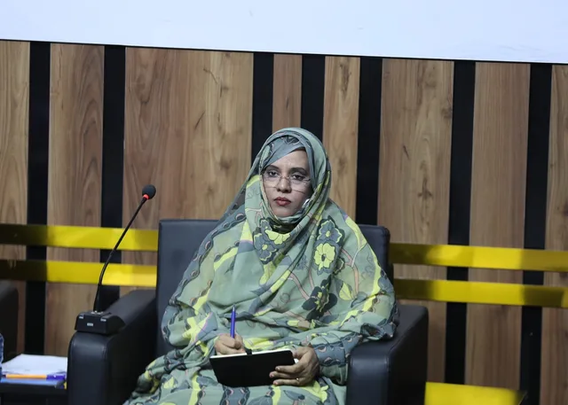 Mauritania's education minister seated on a stage holding a pen and notebook