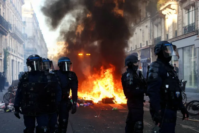 Helmeted police officers in front of a barricade fire in a Paris street