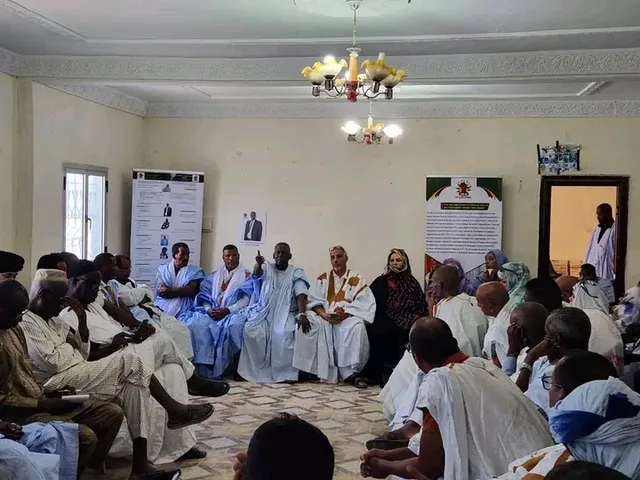 Participants seated in a circle in a meeting hall under political banners