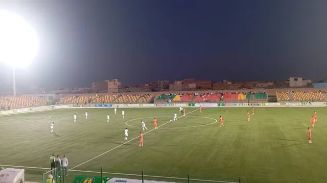 FC Nouadhibou players in orange during a night match at a stadium in Nouakchott