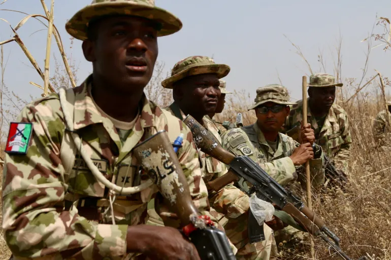 Nigerian soldiers in camouflage and bush hats holding rifles among dry grass during an exercise, file photo
