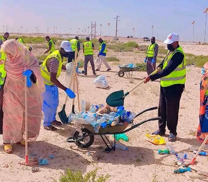 Workers in high-visibility vests collect plastic waste into a wheelbarrow