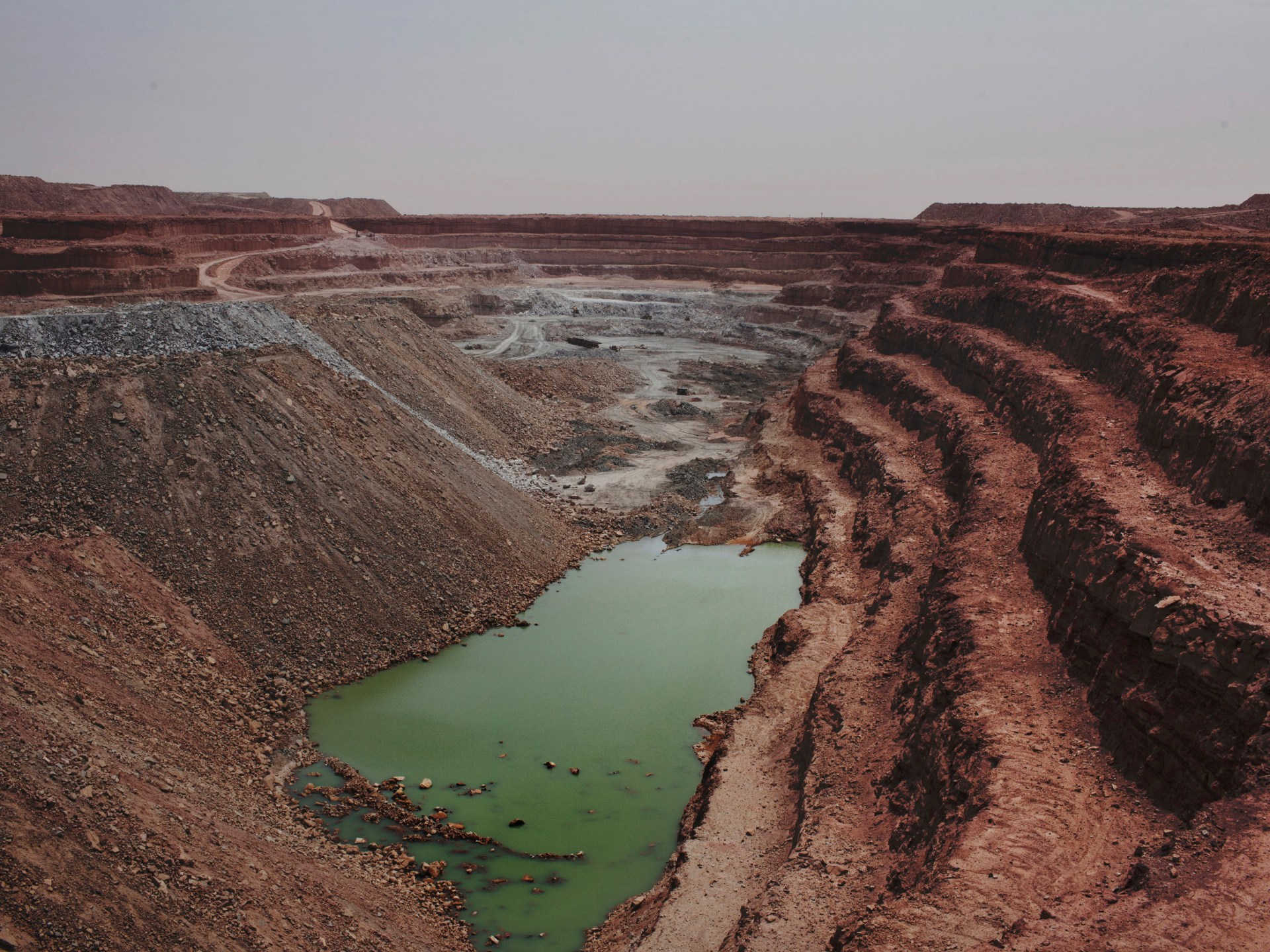 A vast open-pit mine with red earth terraces and a green pool at the bottom, in the desert, file photo