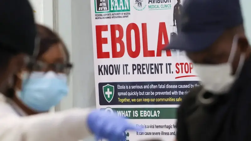 A masked health worker in front of an Ebola awareness poster
