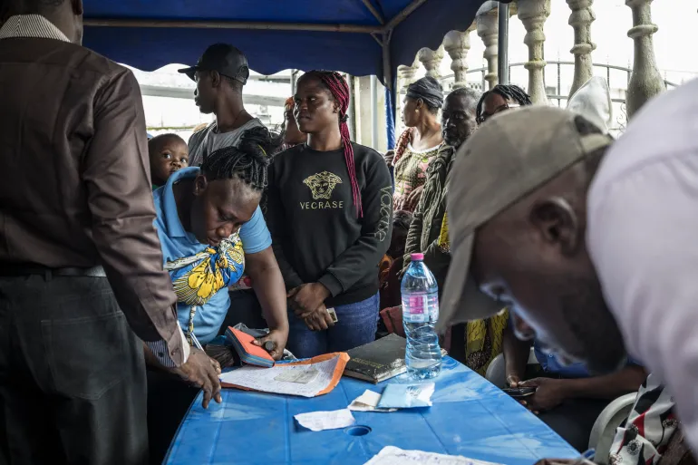Voters queue at a table under a blue canopy as officials record details at a polling station in Cameroon
