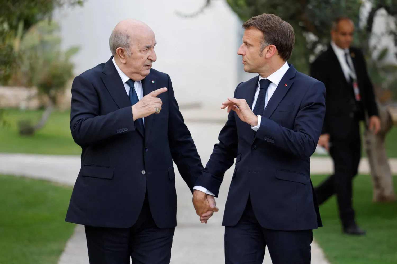 Abdelmadjid Tebboune and Emmanuel Macron walking side by side in a garden