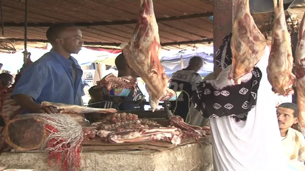Carcasses hanging at a butcher's stall in a market, a seller behind the counter, file photo