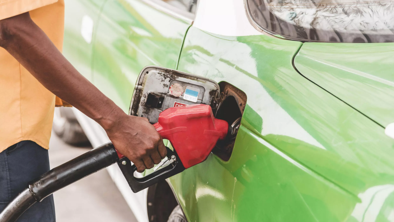 A hand holds a red fuel nozzle in the tank of a green car, illustrative file photo
