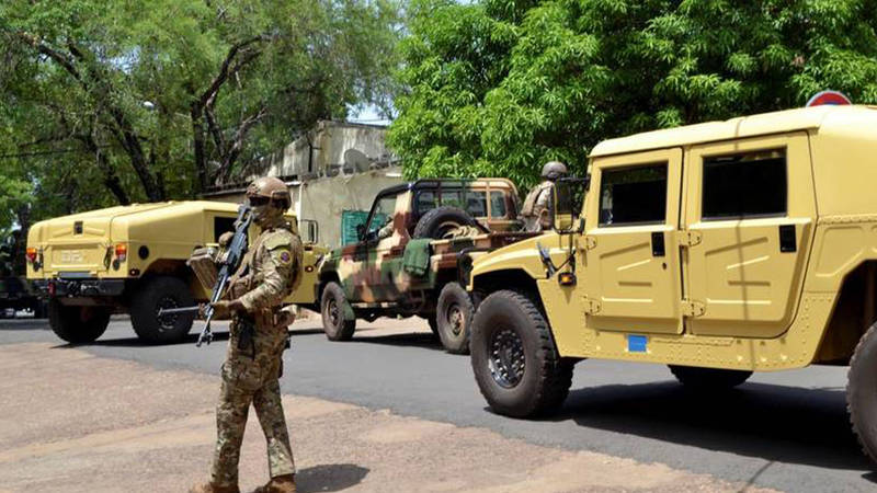 An armed Malian soldier standing near military vehicles in a street