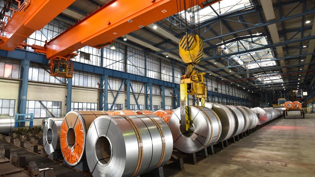 Steel coils lined up inside a factory under a yellow overhead crane, file illustration