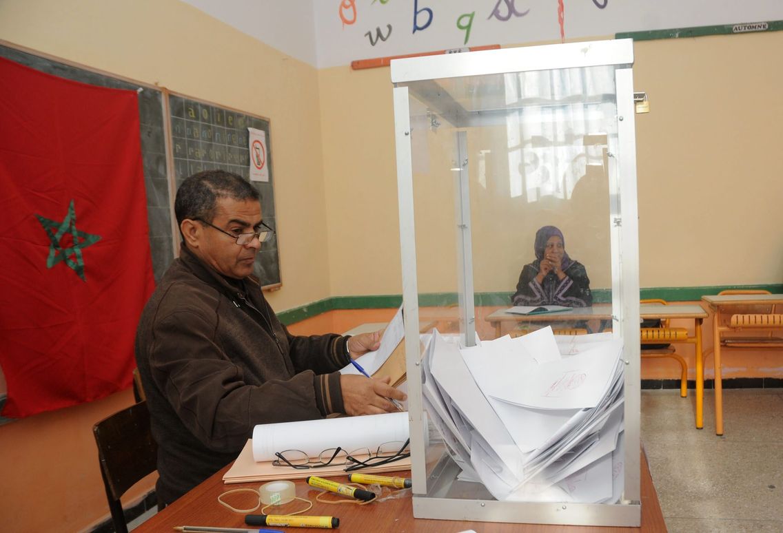 An official sitting next to a transparent ballot box full of ballots in a classroom used as a polling station in Morocco, file photo