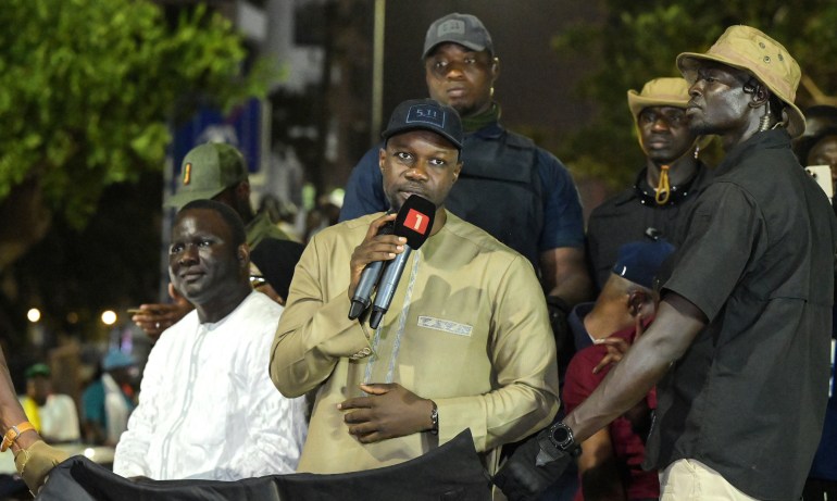Ousmane Sonko speaks into microphones at a night rally