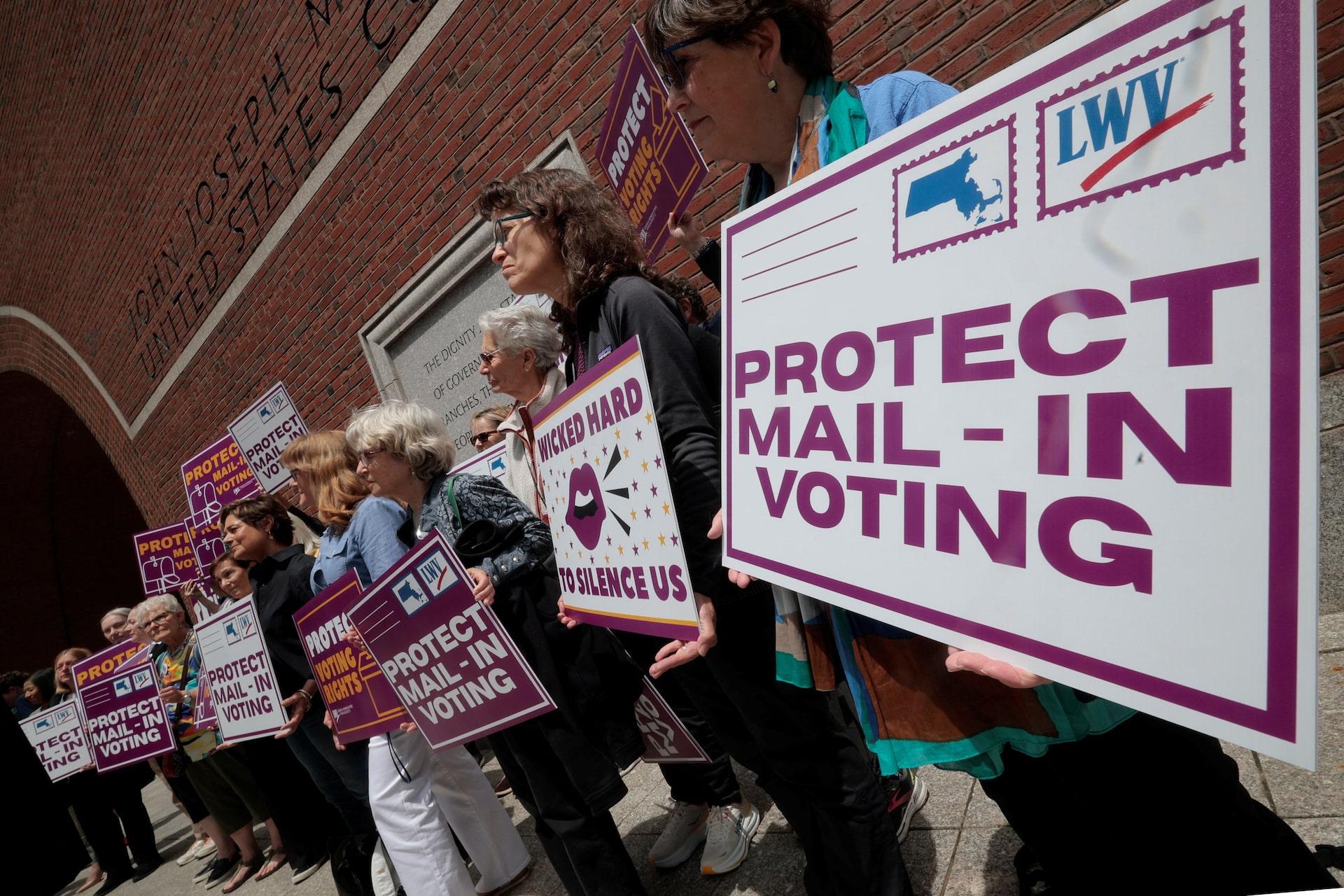 Demonstrators hold signs supporting mail-in voting